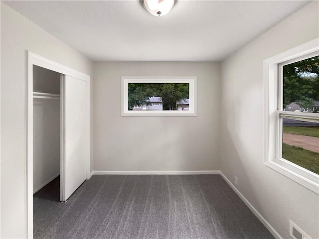 unfurnished bedroom featuring dark colored carpet and multiple windows