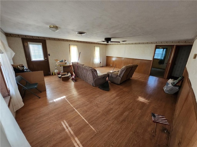 living room with a textured ceiling, wood walls, hardwood / wood-style floors, and ceiling fan