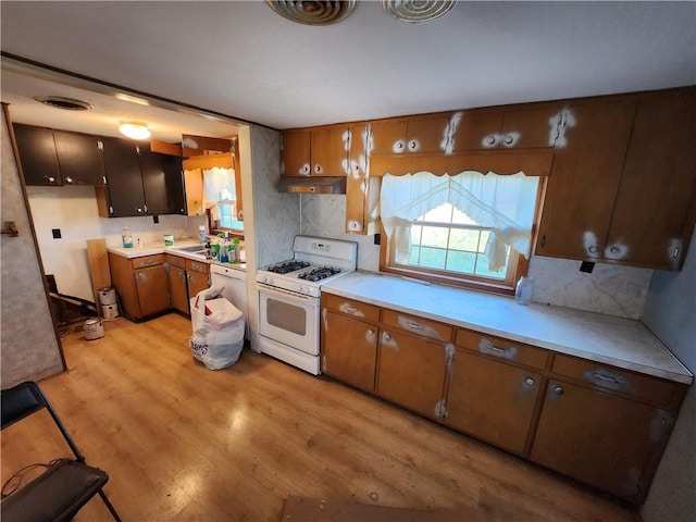 kitchen featuring decorative backsplash, light hardwood / wood-style floors, sink, and white gas range oven