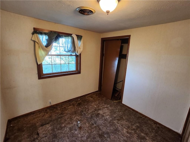 unfurnished bedroom featuring a textured ceiling, a closet, and dark colored carpet