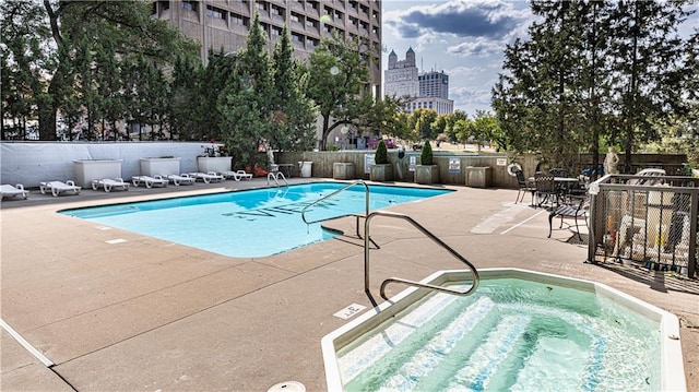 pool with a view of city, a community hot tub, a patio area, and fence