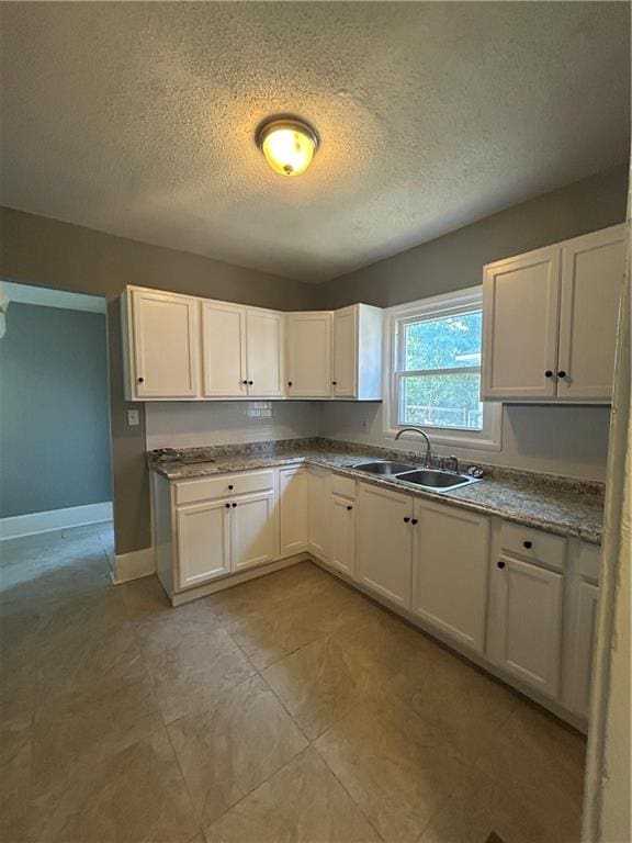 kitchen with white cabinets, a textured ceiling, sink, and light tile patterned flooring