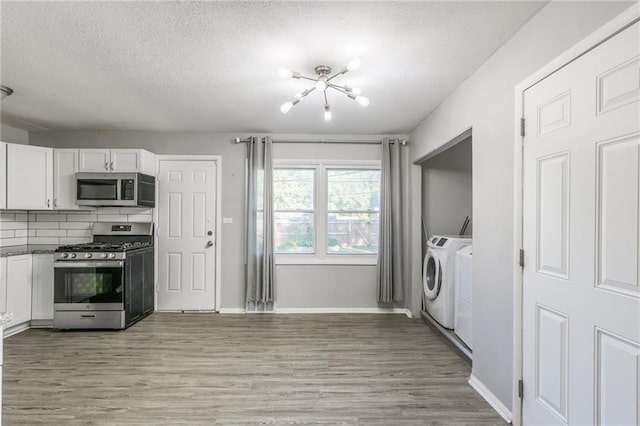 kitchen with light hardwood / wood-style flooring, appliances with stainless steel finishes, washing machine and dryer, and white cabinetry