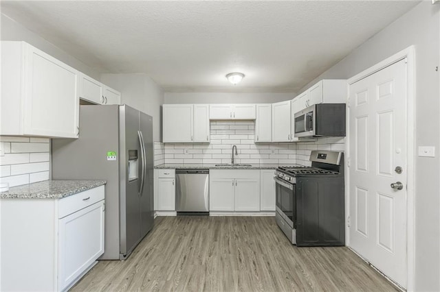 kitchen featuring appliances with stainless steel finishes, white cabinets, light stone countertops, light wood-type flooring, and sink