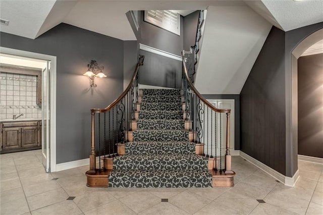 staircase with lofted ceiling, sink, and tile patterned floors