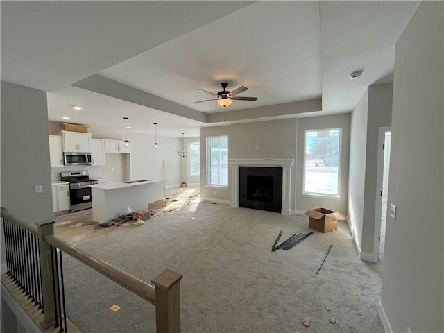 carpeted living room featuring ceiling fan with notable chandelier and a tray ceiling