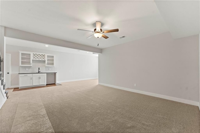 unfurnished living room with indoor wet bar, visible vents, ceiling fan, and baseboards