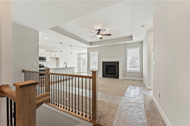 interior space with baseboards, a tiled fireplace, ceiling fan, a tray ceiling, and carpet flooring