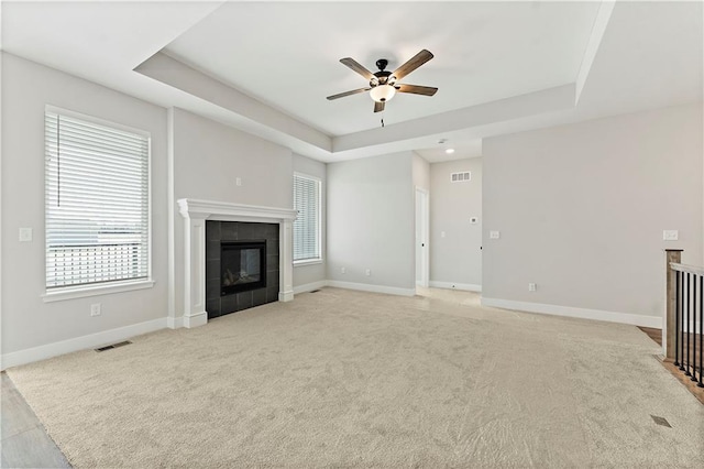 unfurnished living room with a tile fireplace, a raised ceiling, visible vents, and baseboards