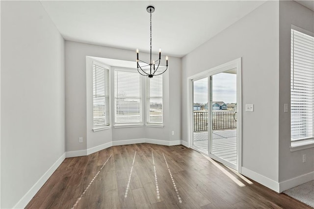 unfurnished dining area with baseboards, a chandelier, a wealth of natural light, and wood finished floors