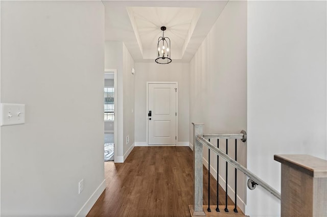 entryway featuring dark wood-style floors, baseboards, a raised ceiling, and an inviting chandelier