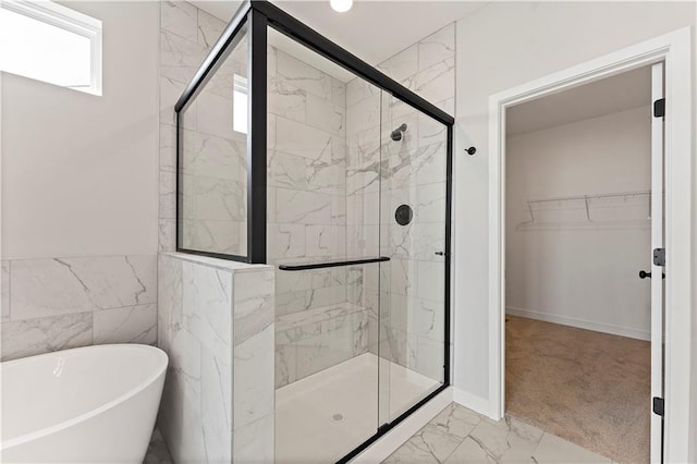 bathroom featuring marble finish floor, a spacious closet, a stall shower, and a freestanding tub