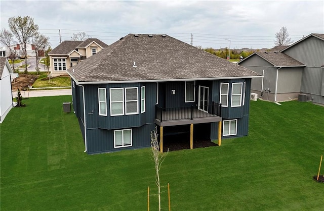 rear view of house featuring a wooden deck, a lawn, a shingled roof, and central AC unit
