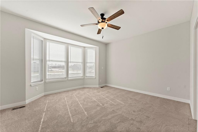 empty room featuring visible vents, a ceiling fan, baseboards, and light colored carpet