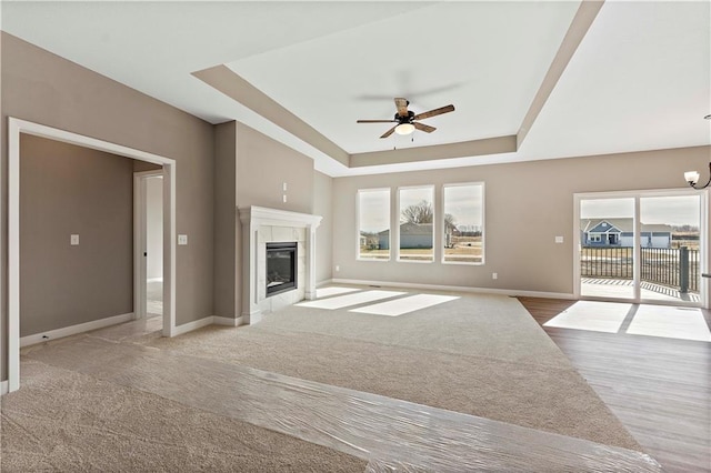 unfurnished living room with ceiling fan with notable chandelier, a tray ceiling, a fireplace, and baseboards