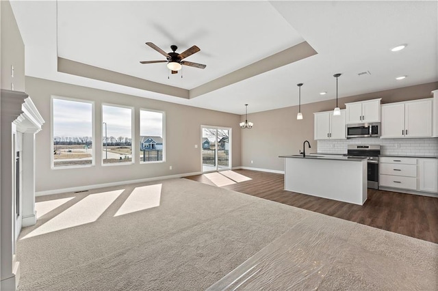 kitchen featuring open floor plan, stainless steel appliances, dark countertops, and a raised ceiling