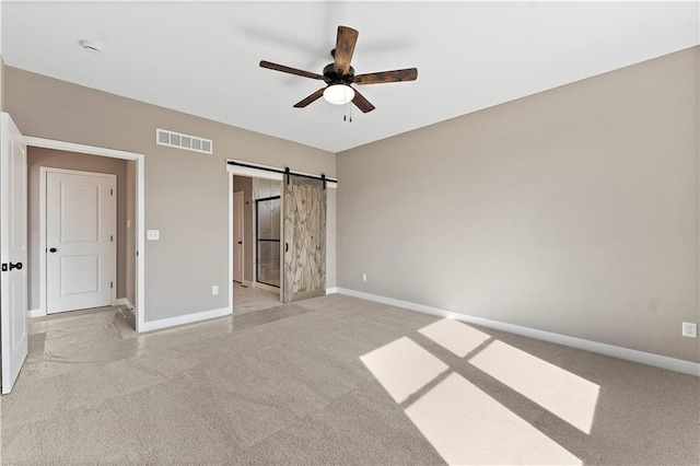 unfurnished bedroom with light colored carpet, visible vents, baseboards, and a barn door