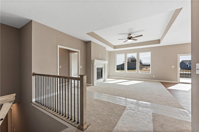 living area featuring baseboards, a tile fireplace, ceiling fan, a tray ceiling, and carpet floors