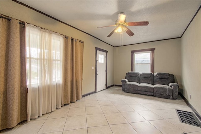 living area with light tile patterned floors, visible vents, ornamental molding, ceiling fan, and a textured ceiling