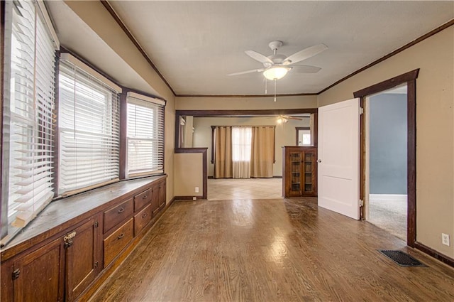 unfurnished living room with baseboards, visible vents, a ceiling fan, ornamental molding, and wood finished floors