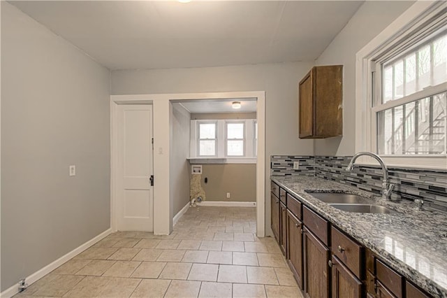 kitchen with stone counters, a sink, backsplash, and baseboards