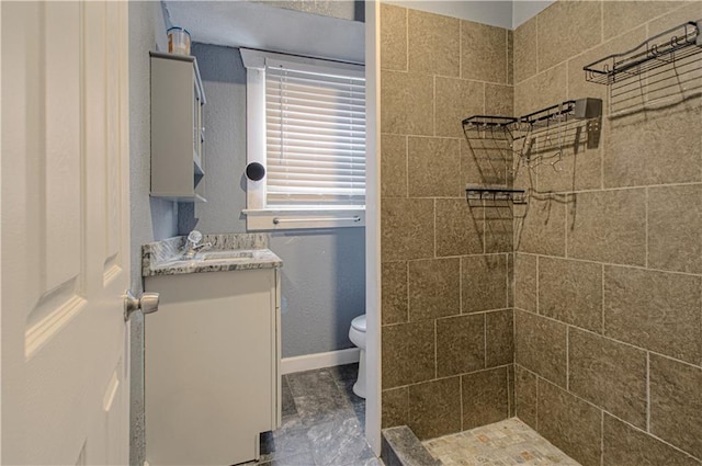 bathroom featuring toilet, baseboards, a tile shower, and vanity