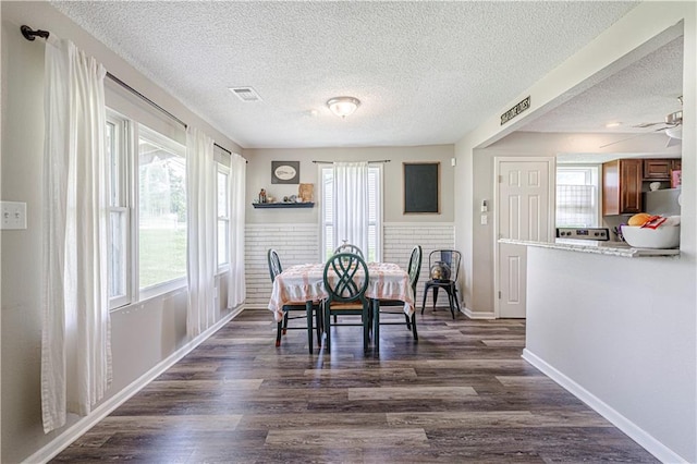 dining space featuring ceiling fan, brick wall, plenty of natural light, and dark hardwood / wood-style flooring