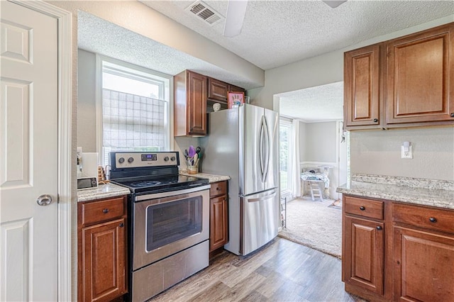 kitchen featuring light stone countertops, a textured ceiling, stainless steel appliances, and light hardwood / wood-style floors