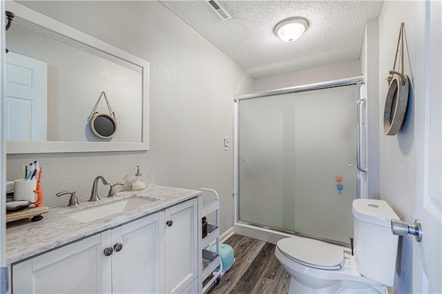 bathroom featuring vanity, wood-type flooring, a textured ceiling, toilet, and a shower with door