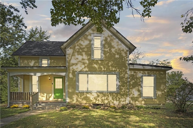 back house at dusk featuring covered porch and a lawn