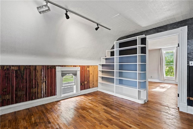 unfurnished living room with a textured ceiling, hardwood / wood-style flooring, wooden walls, and a healthy amount of sunlight