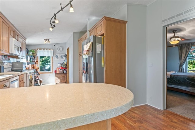 kitchen with dishwashing machine, white microwave, light wood-style flooring, freestanding refrigerator, and light countertops