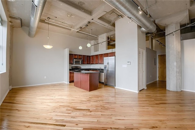 kitchen featuring light hardwood / wood-style floors, a center island, a towering ceiling, and stainless steel appliances