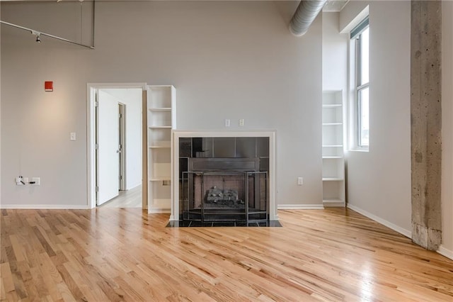 unfurnished living room with light wood-type flooring, a fireplace, and a towering ceiling