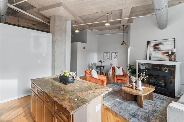 kitchen with light stone countertops, light wood-type flooring, a center island, and hanging light fixtures