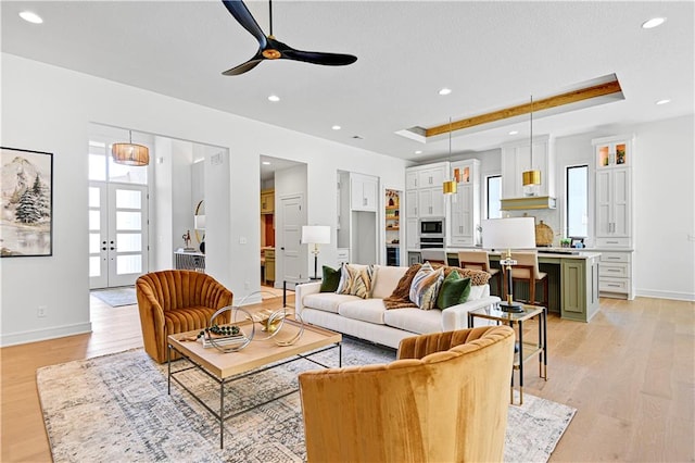 living room featuring ceiling fan, a tray ceiling, french doors, and light hardwood / wood-style floors