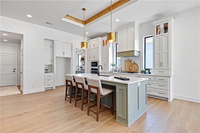 kitchen featuring light hardwood / wood-style floors, white cabinetry, decorative light fixtures, a center island with sink, and sink