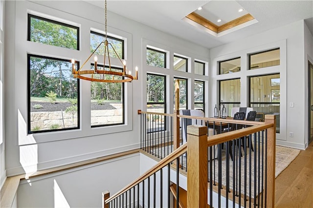 hallway featuring a notable chandelier, a high ceiling, a tray ceiling, and light hardwood / wood-style floors