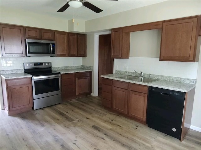 kitchen with stainless steel appliances, backsplash, a sink, light wood-style flooring, and ceiling fan