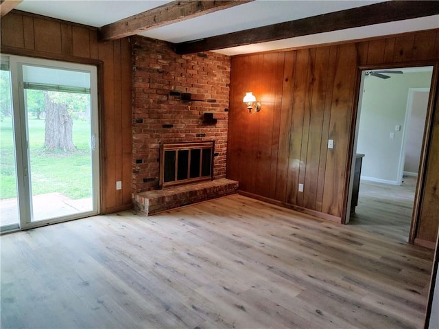 unfurnished living room featuring light hardwood / wood-style floors, wood walls, and a brick fireplace