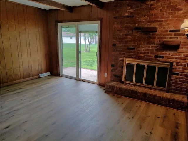unfurnished living room featuring wooden walls, wood finished floors, beam ceiling, and a brick fireplace