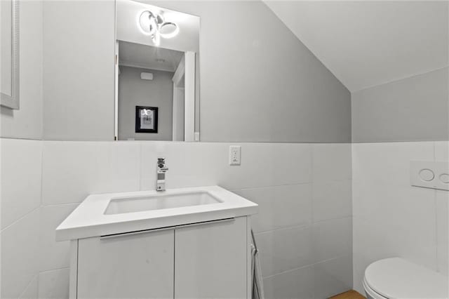 bathroom with lofted ceiling, vanity, tile walls, and toilet