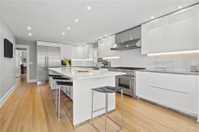 kitchen featuring high end appliances, light hardwood / wood-style flooring, a kitchen island, a kitchen bar, and white cabinetry