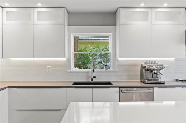 kitchen with stainless steel dishwasher, decorative backsplash, white cabinetry, and sink