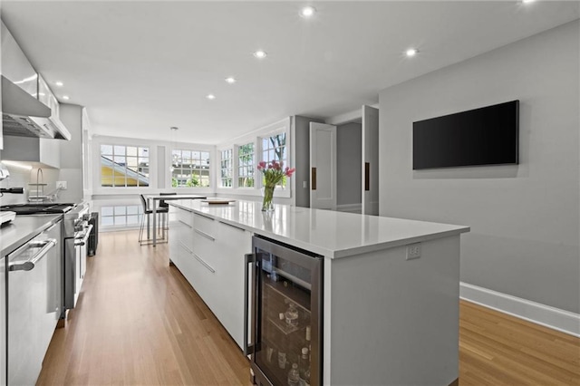 kitchen featuring wine cooler, a kitchen island, light hardwood / wood-style floors, white cabinetry, and stainless steel appliances