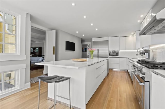 kitchen featuring white cabinetry, a center island, built in appliances, extractor fan, and light wood-type flooring