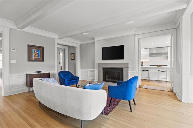 living room featuring beam ceiling, light hardwood / wood-style flooring, and ornamental molding