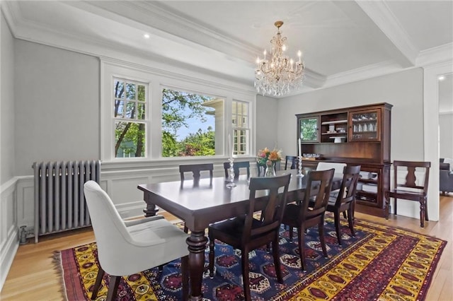 dining space featuring light wood-type flooring, ornamental molding, radiator, and a chandelier