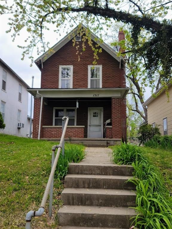 view of front facade with a porch, a front yard, and brick siding