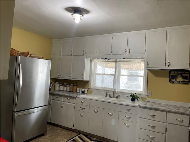 kitchen featuring white cabinetry, light countertops, a sink, and freestanding refrigerator